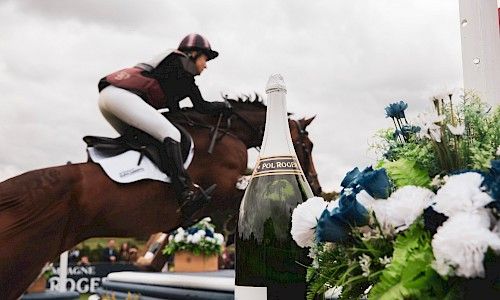 Burghley Horse Trials horse jumping with champagne bottle in the foreground